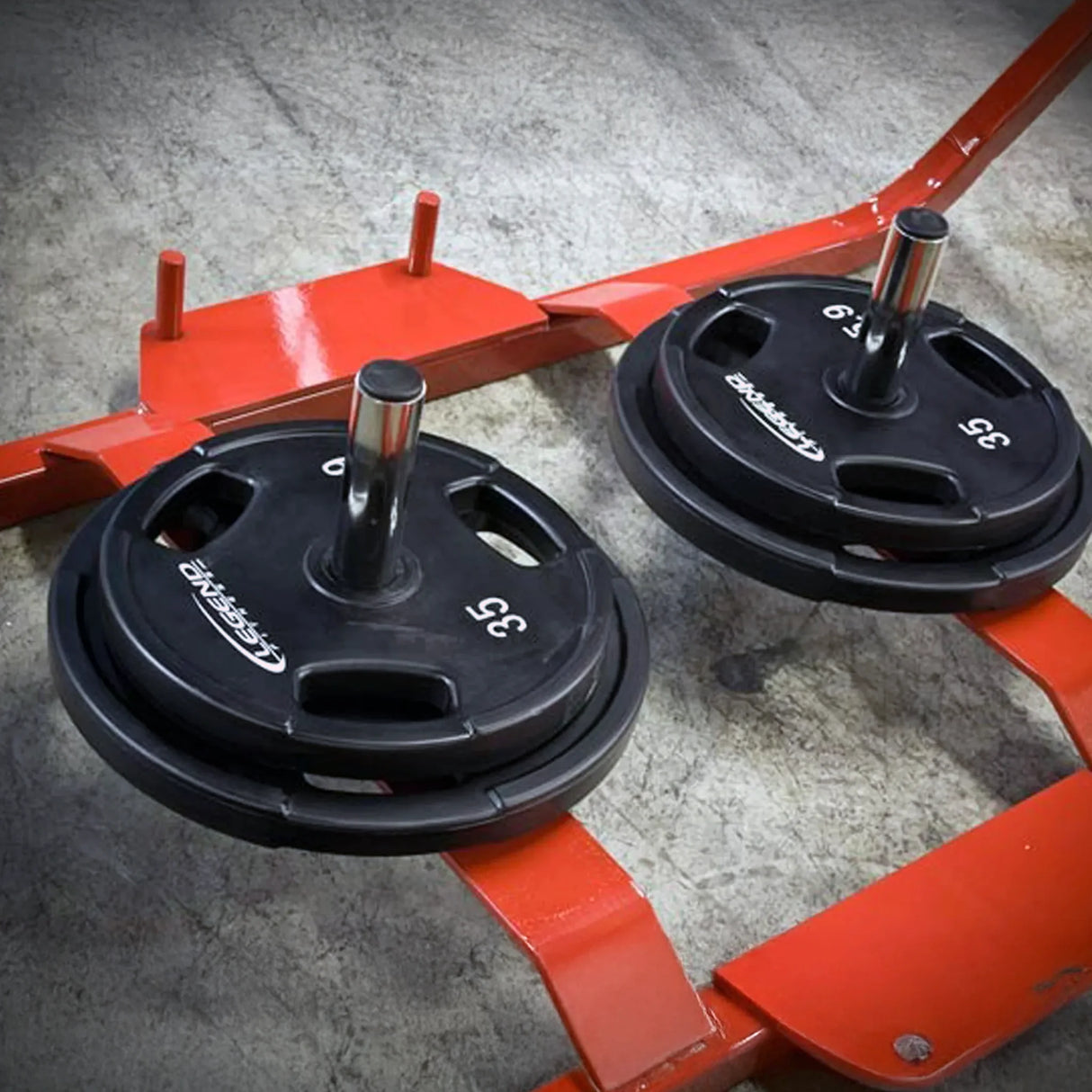 Two black weight plates on a red metal frame with a concrete floor background
