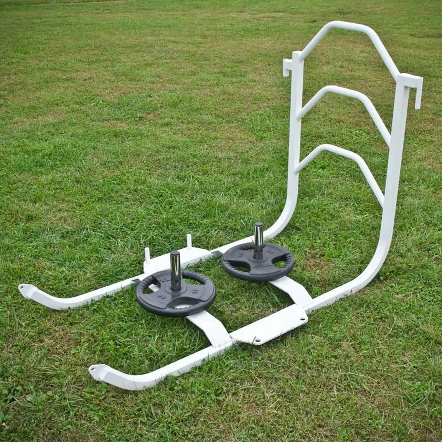 A white metal push sled with black weight lifting plates on it on grass