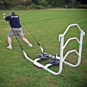 A man pulling a white metal sled on grass by two black straps