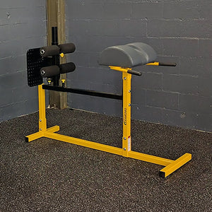 A yellow glute ham developer with black pads in a gym setting