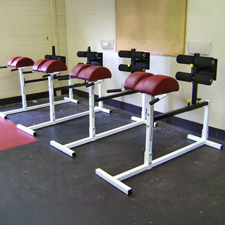 Four white Legend Fitness glute ham developers with red pads in a gym