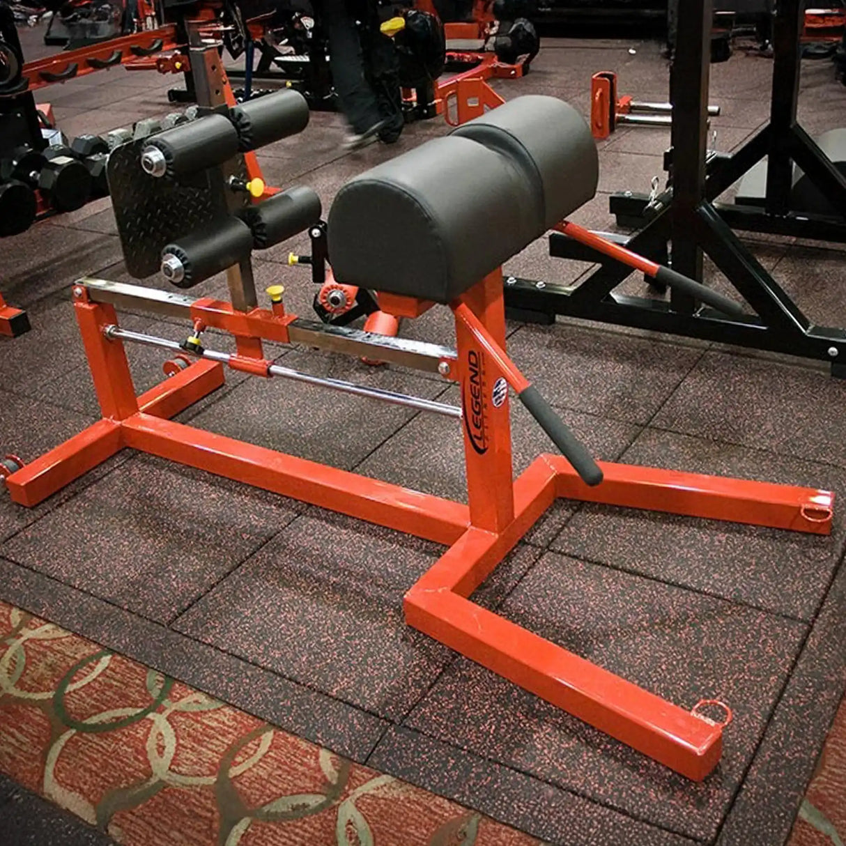 A red Legend Fitness glute ham developer with black pads in a gym setting