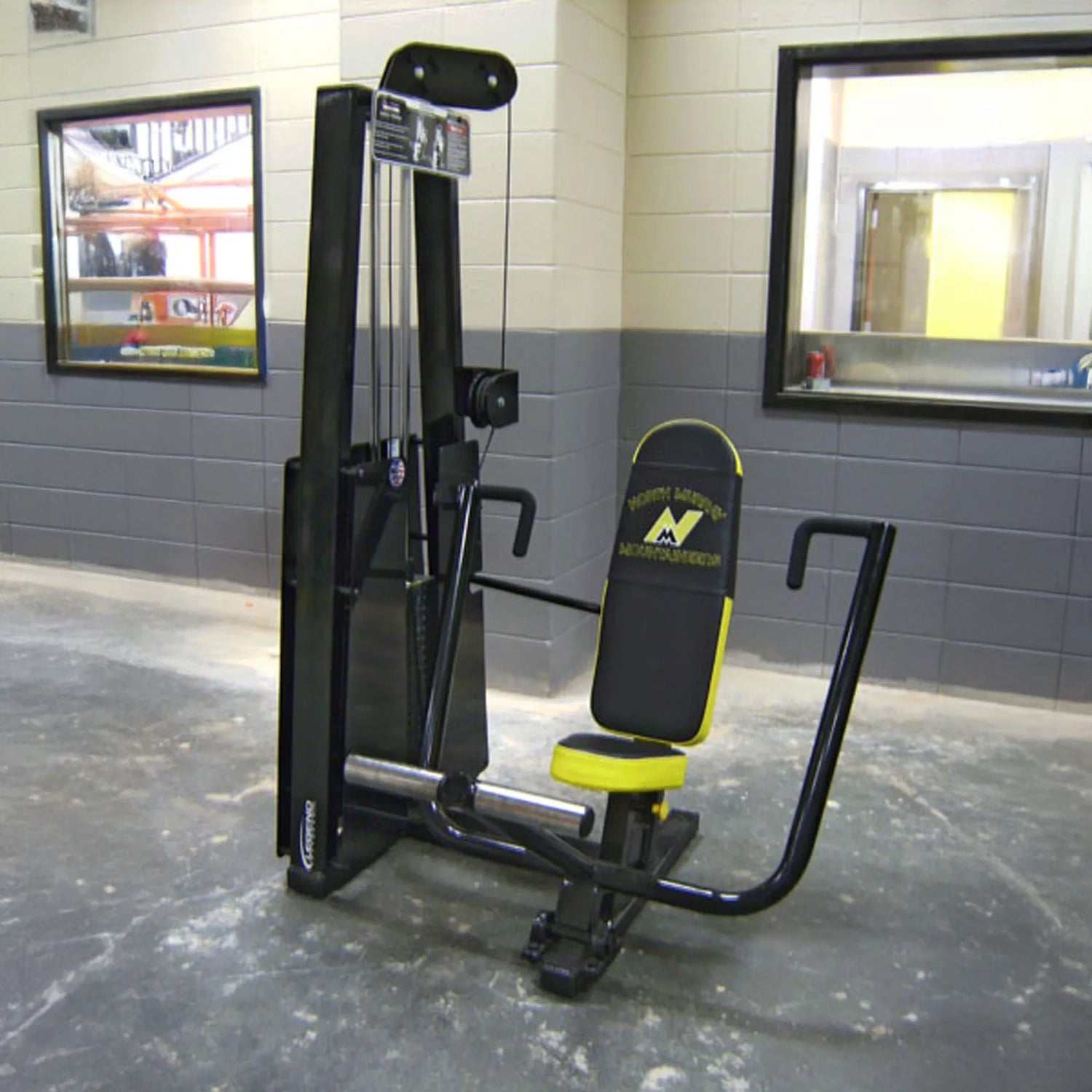 The Legend Fitness 900 Chest Press Machine by Legend Fitness in black and yellow is set up in a gym with gray and white walls, a concrete floor, and windows in the background.