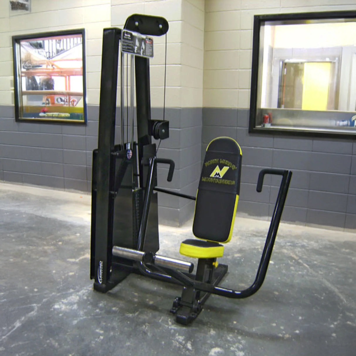 The Legend Fitness 900 Chest Press Machine by Legend Fitness in black and yellow is set up in a gym with gray and white walls, a concrete floor, and windows in the background.