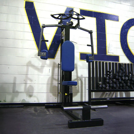 The Legend Fitness 901 Pec Deck Machine by Legend Fitness, in blue and black, is placed before a wall with large letters and a dumbbell rack. It’s designed for effective chest and arm exercises.