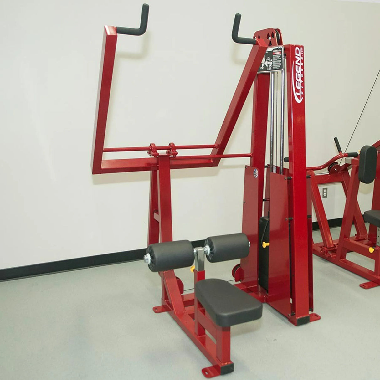 The Legend Fitness 903 Lever Lat Pulldown Machine by Legend Fitness, featuring red seating, padded rollers, and handles for upper body workouts, stands against a light-colored wall in the gym.