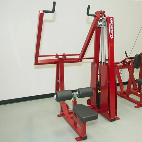 The Legend Fitness 903 Lever Lat Pulldown Machine by Legend Fitness, featuring red seating, padded rollers, and handles for upper body workouts, stands against a light-colored wall in the gym.