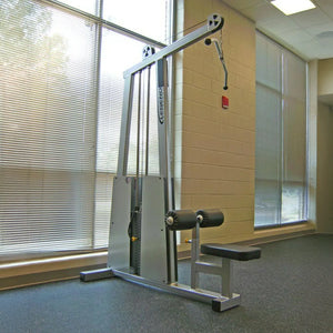 A Legend Fitness 905 Lat Pulldown Machine by Legend Fitness stands near a beige wall in a gym with large windows, blinds, black rubber flooring, and abundant natural light.
