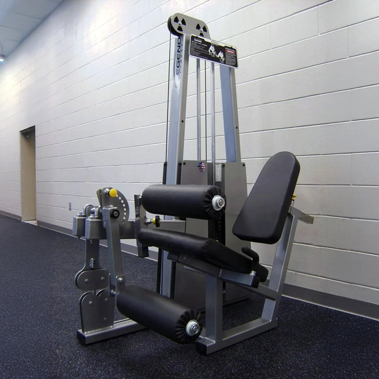 The Legend Fitness 918 Leg Extension / Leg Curl Combo Machine by Legend Fitness features padded seats, supportive rollers, and an adjustable weight stack, shown here in an empty gym with gray walls and black flooring.