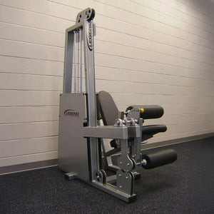 The Legend Fitness 918 Leg Extension / Leg Curl Combo Machine by Legend Fitness, featuring padded black rollers and a silver frame, is set against a beige brick wall on a dark speckled gym floor.