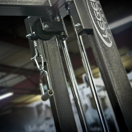 A close-up of the Legend Fitness 919 Cable Crossover Machine highlights its metal handle attachment, weight stack, and branded frame, with a blurred background.