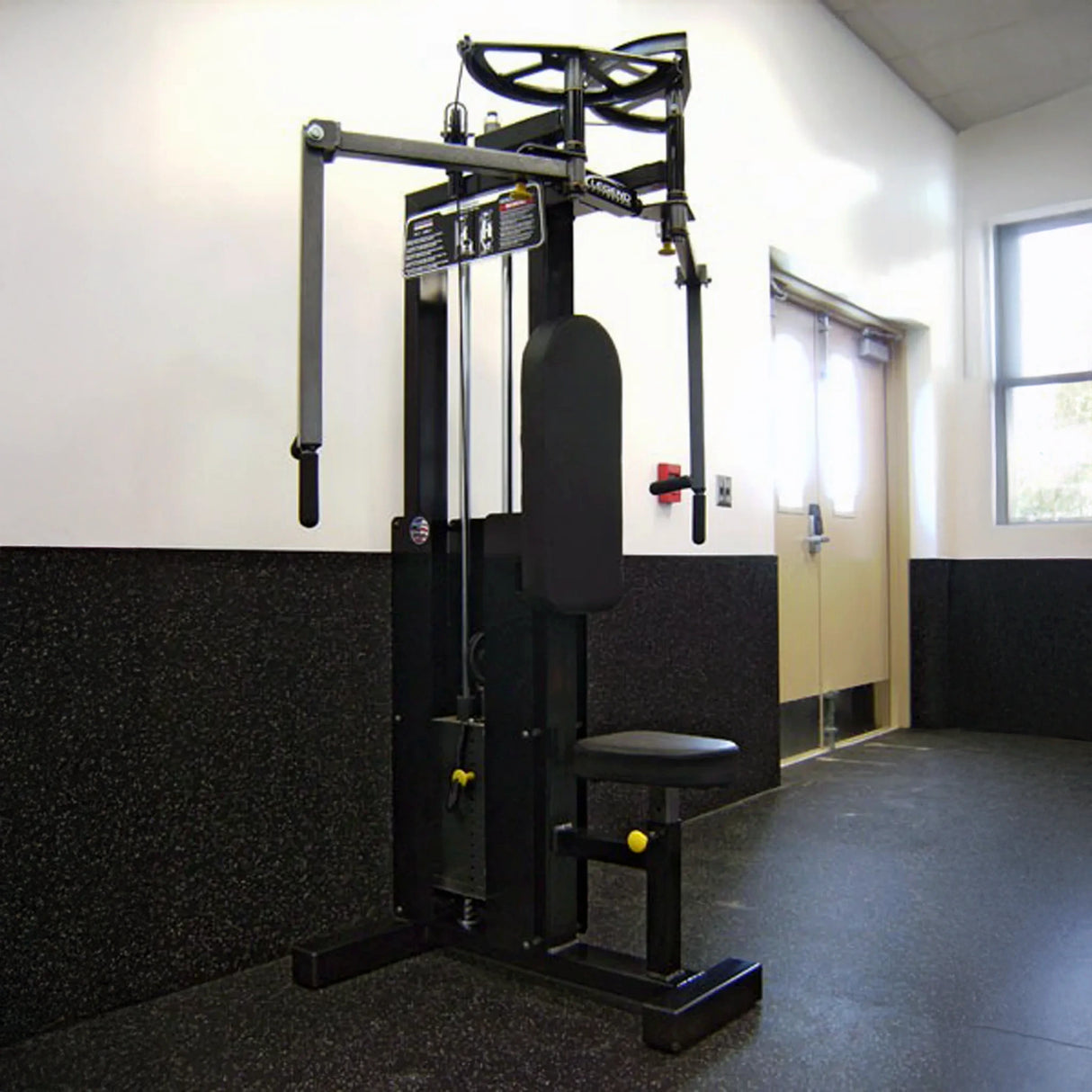 A Legend Fitness 942 Rear Delt / Pec Combo Machine with seat and padded arms is in a clean, well-lit gym room near a door and window. The gym features white walls, dark speckled lower panels, and black rubber flooring.