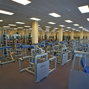 A spacious gym features multiple Legend Fitness 943 Neck Machine machines and benches in rows under bright overhead lights, with mirrors lining the back wall.