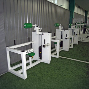 Four Legend Fitness 943 Neck Machines with green padding are lined up on artificial turf beside a corrugated metal wall in an indoor gym.