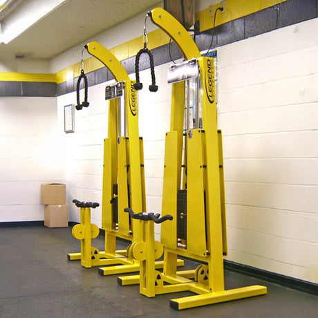 Two Legend Fitness 946 Standing Bicep / Tricep Combo Machines, tall and bright yellow with black handles, stand side by side against a white and yellow gym wall. Each features seats, pulleys, and boxes stacked in the corner.