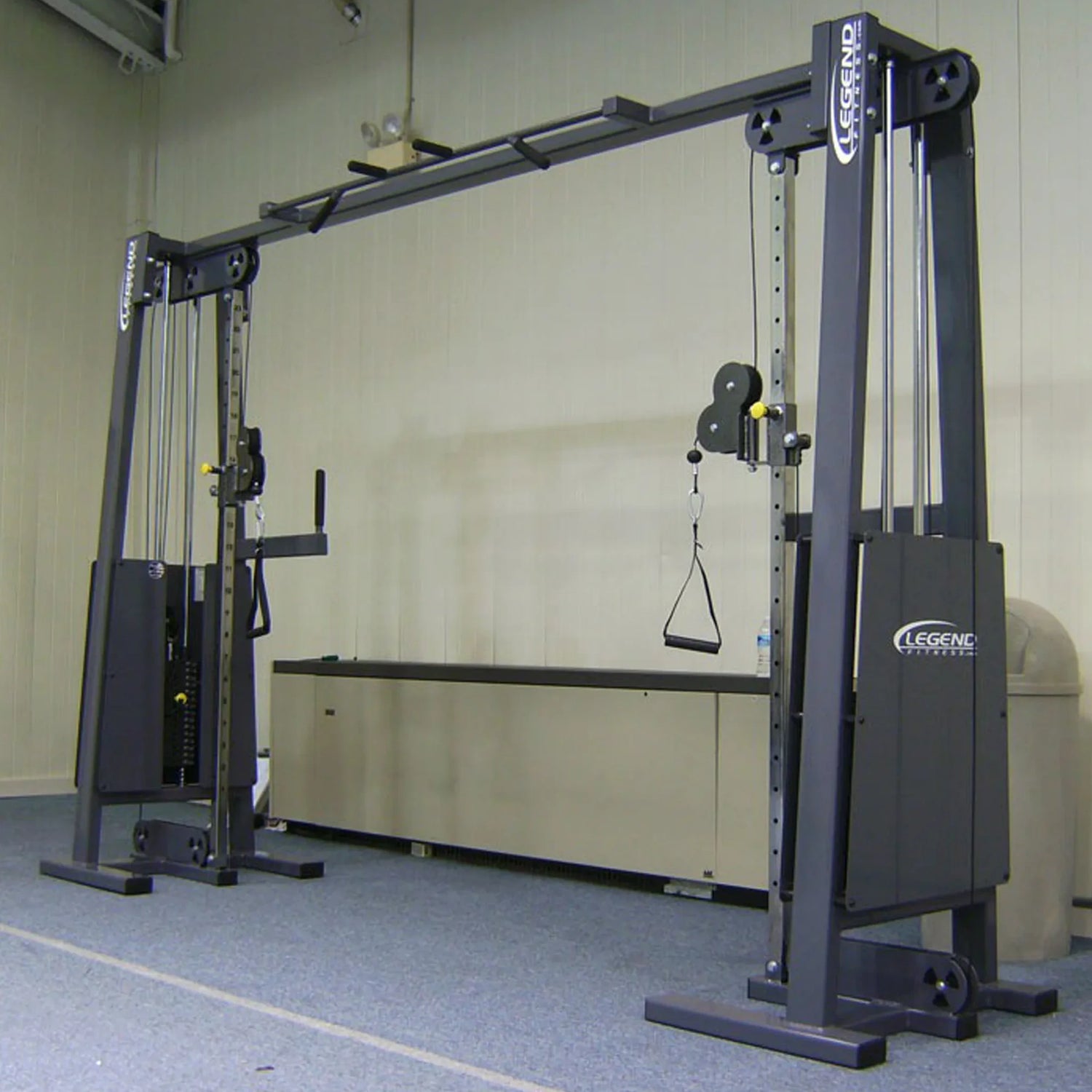 The Legend Fitness 954 Cable Crossover with Adjustable Pulleys and handles stands on a carpeted gym floor with beige walls, featuring the Legend Fitness brand.