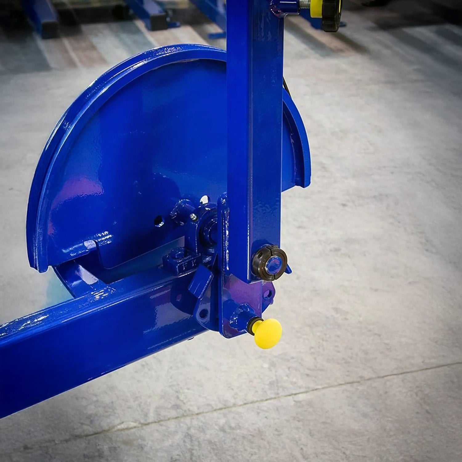 Close-up of the Legend Fitness 957 Low Back / Ab Combo Machine by Legend Fitness, featuring a blue metal frame with bolts, a circular cover, and a yellow knob on the bottom right, positioned on a smooth concrete floor.