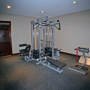 The room features a Legend Fitness 958 Four-Stack Jungle Gym with padded benches and attached cables, plus a hyperextension bench with red resistance bands on carpeted flooring, beige walls, and recessed lighting.