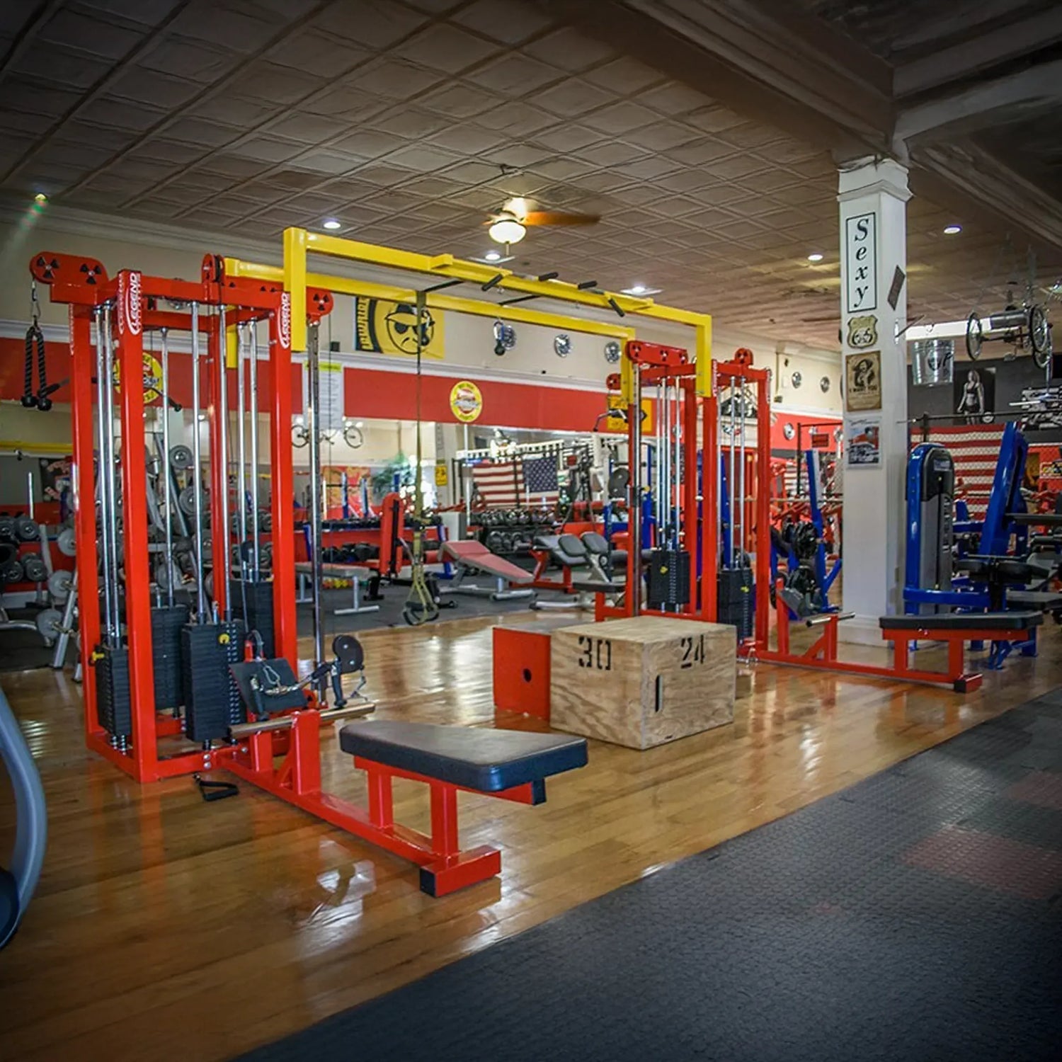 A brightly lit gym featuring the Legend Fitness 959 Eight-Stack Jungle Gym in red and yellow, wooden numbered plyometric boxes, benches, and walls of mirrors reflecting even more Legend Fitness equipment.