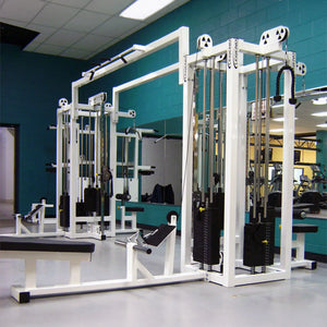 A gym with teal walls showcases the Legend Fitness 959 Eight-Stack Jungle Gym, featuring weight stacks, pulleys, and attachments. Wall mirrors reflect benches and equipment, giving the space a clean, organized look.