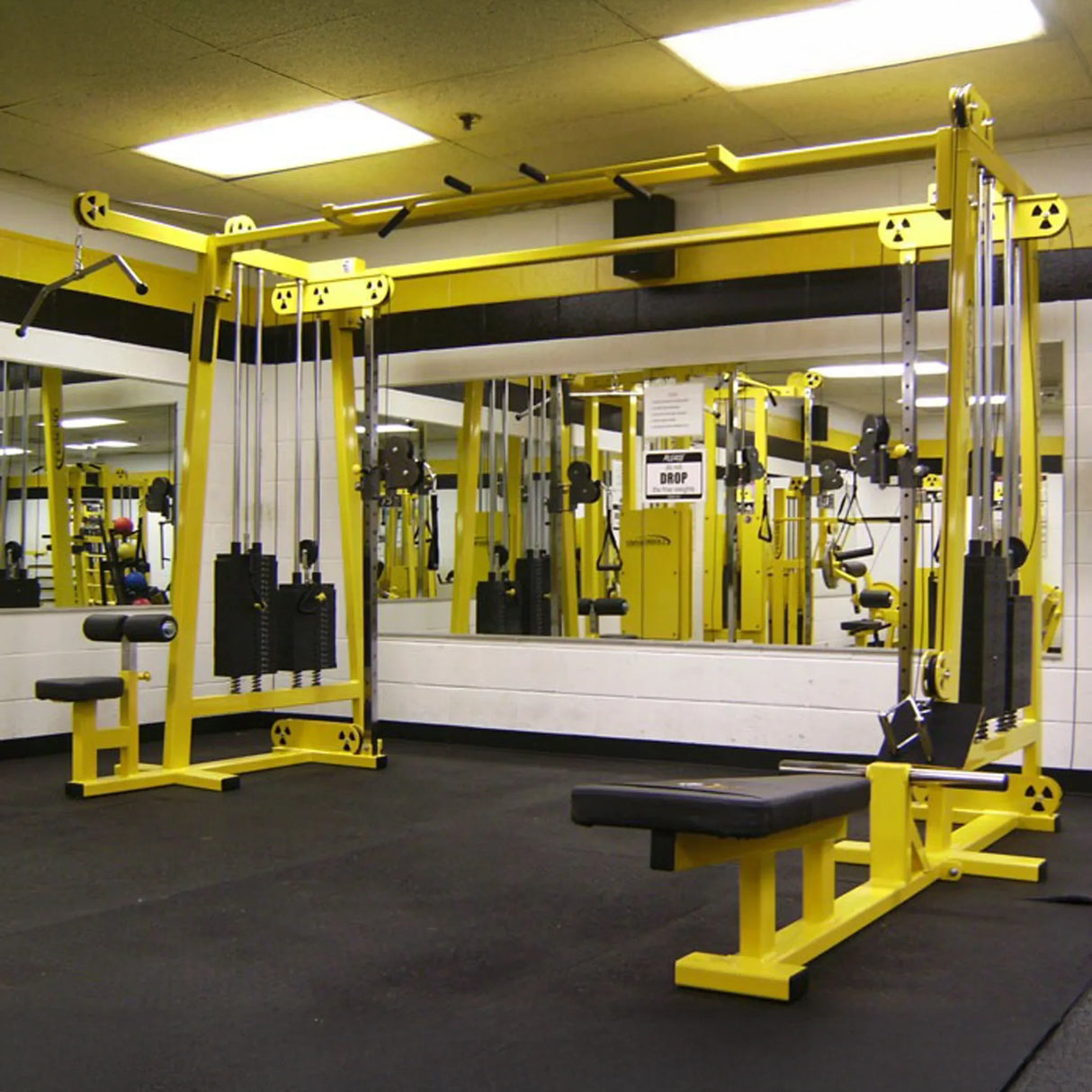 A gym with vibrant yellow Legend Fitness 960 Cable Crossover Plus Machines and other Legend Fitness equipment sits on a black rubber floor, facing large mirrors and white walls.