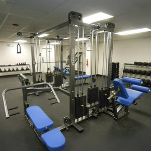 A gym room features the Legend Fitness 965 Combo Jungle Machine with blue seats, weight stacks, and pulleys. Dumbbells by Legend Fitness are neatly arranged on racks along the clean, well-lit walls.