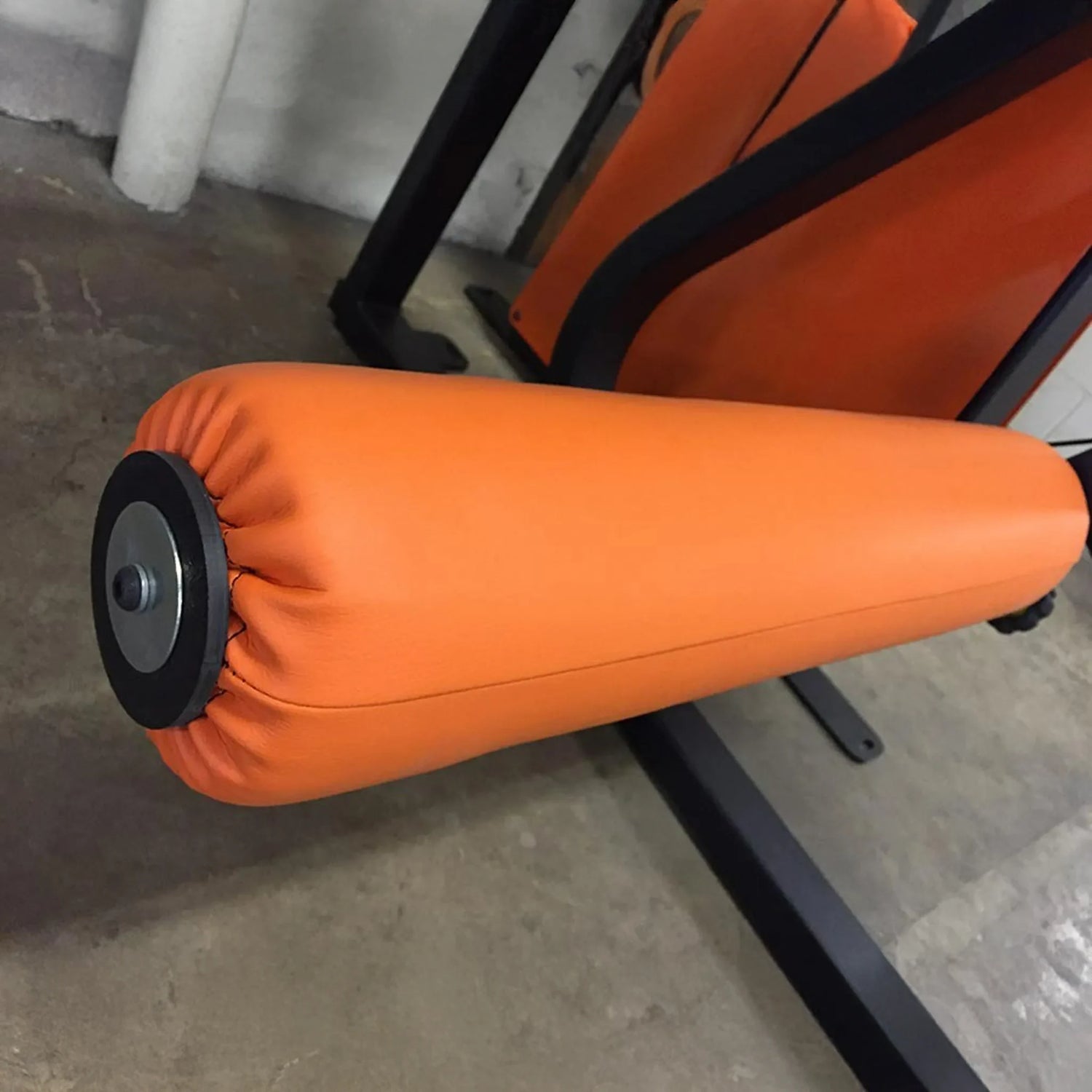 Close-up of the orange padded roller on the Legend Fitness 974 Pro Reverse Back Extension Machine by Legend Fitness, designed for leg exercises and strength training on a concrete floor.