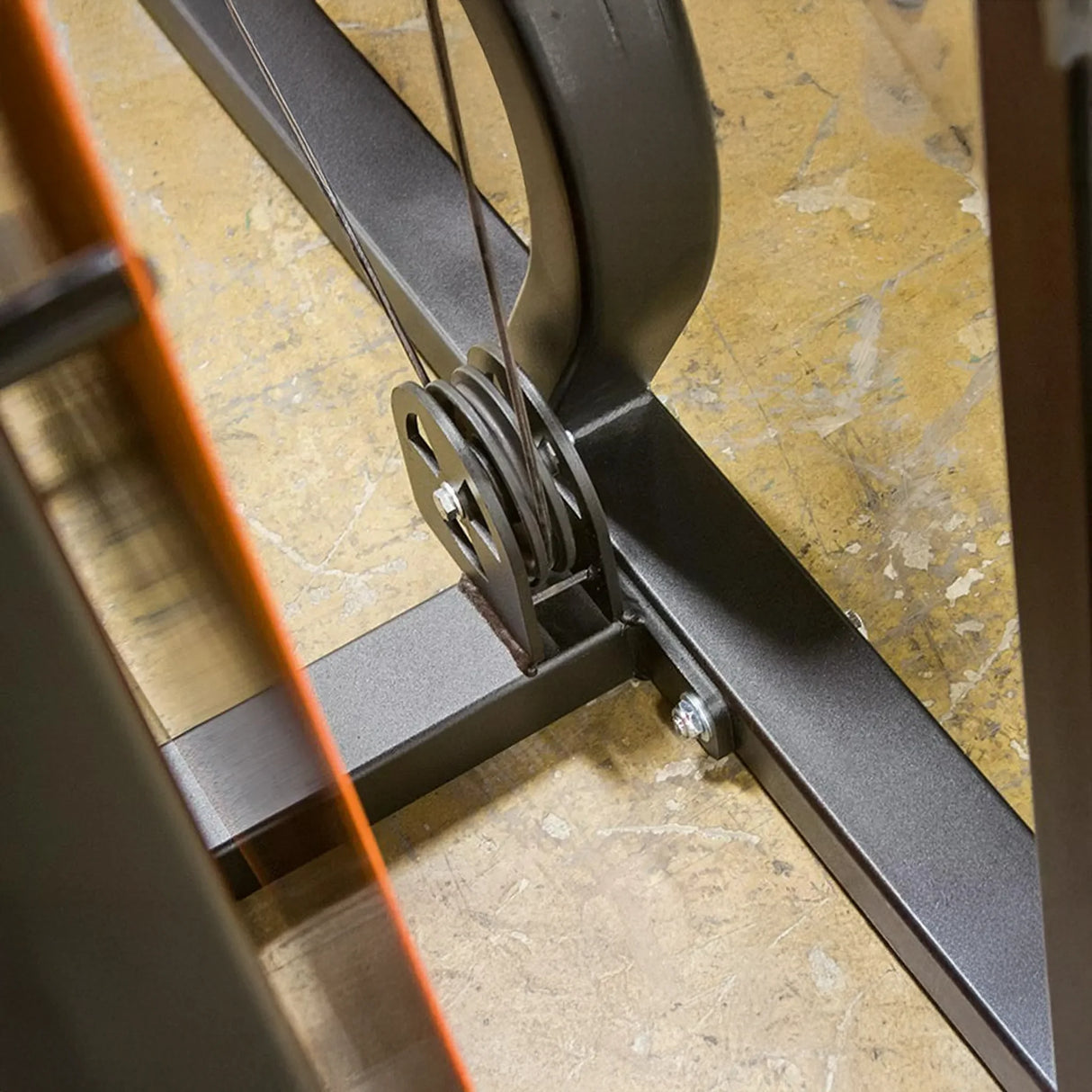 Close-up of the Legend Fitness 974 Pro Reverse Back Extension Machine's metal frame, pulley system, and cables on a yellowish textured floor—equipment by Legend Fitness.