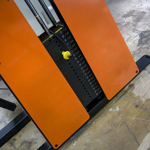 A close-up of the Legend Fitness 974 Pro Reverse Back Extension Machine shows a yellow pin in black weight plates, with the worn, textured floor in the background.