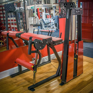 The Legend Fitness 974 Pro Reverse Back Extension Machine by Legend Fitness, in red and black, stands on a wooden gym floor with mirrors and various fitness equipment in the background.