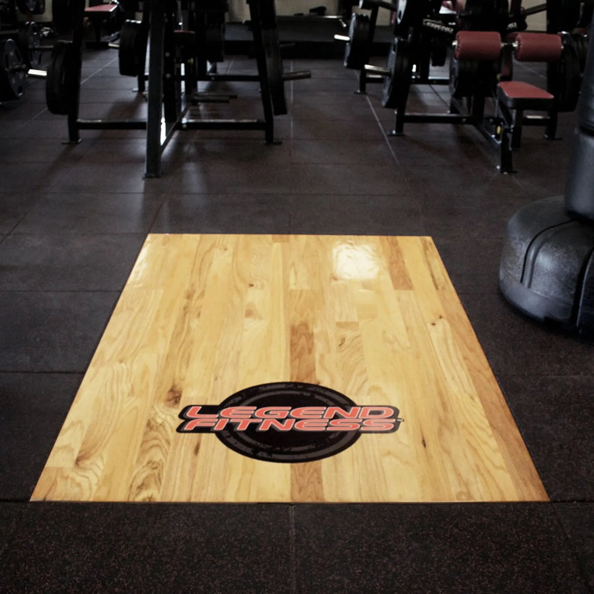 Wooden floor platform surrounded by rubber tiles and gym equipment with a Legend Fitness logo on the wooden portion