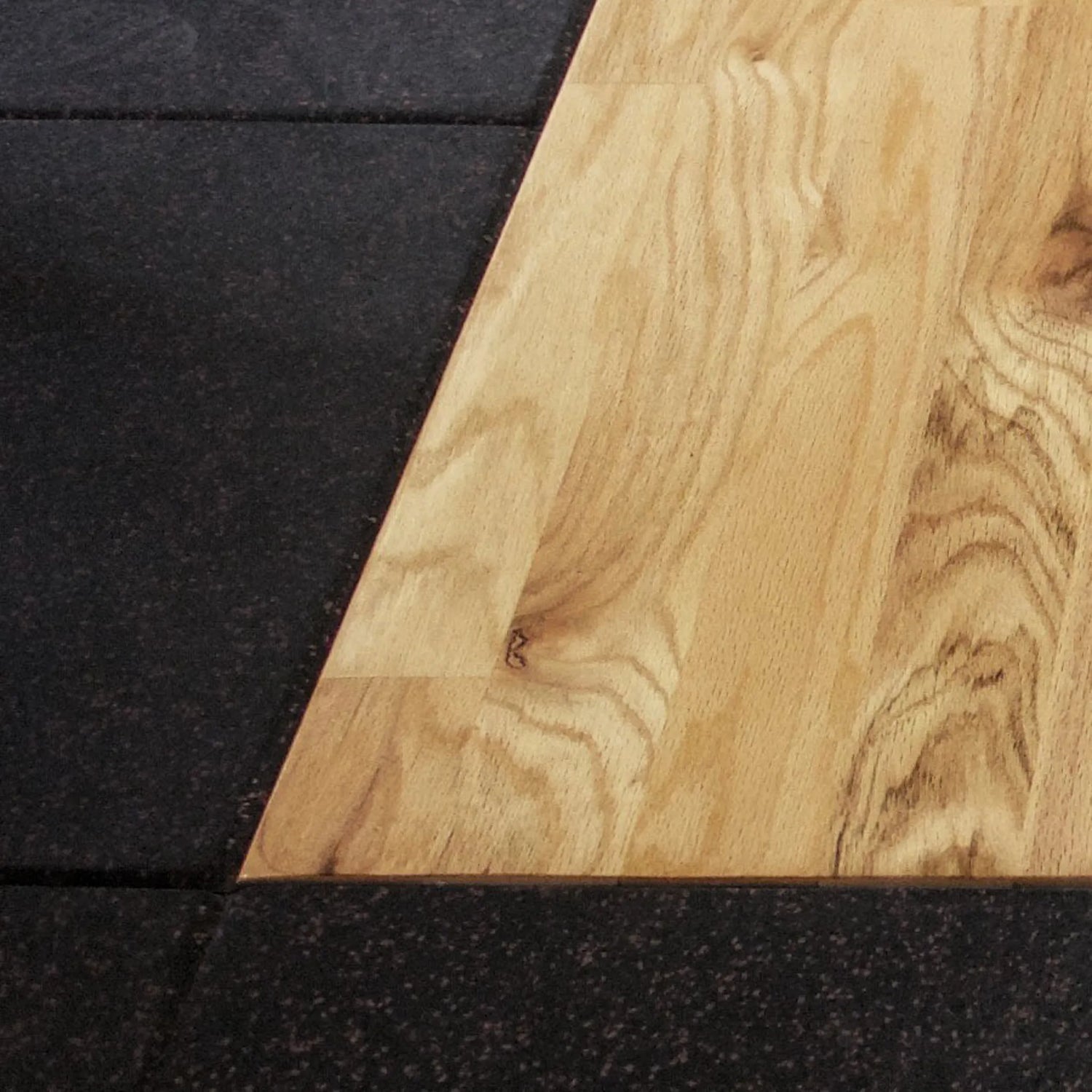 Close-up of a wooden platform corner surrounded by black rubber tiles