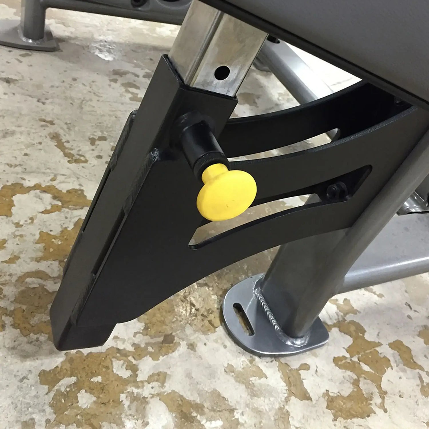 Close-up of a black metal bracket with a yellow knob on a concrete surface