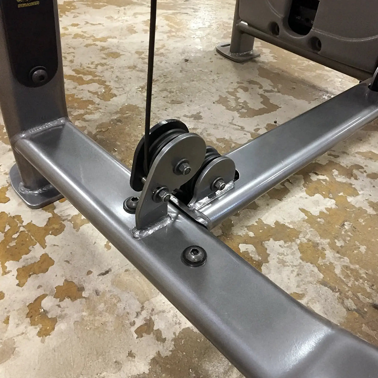 Metal pulley system mounted to a gray metal frame on a concrete floor
