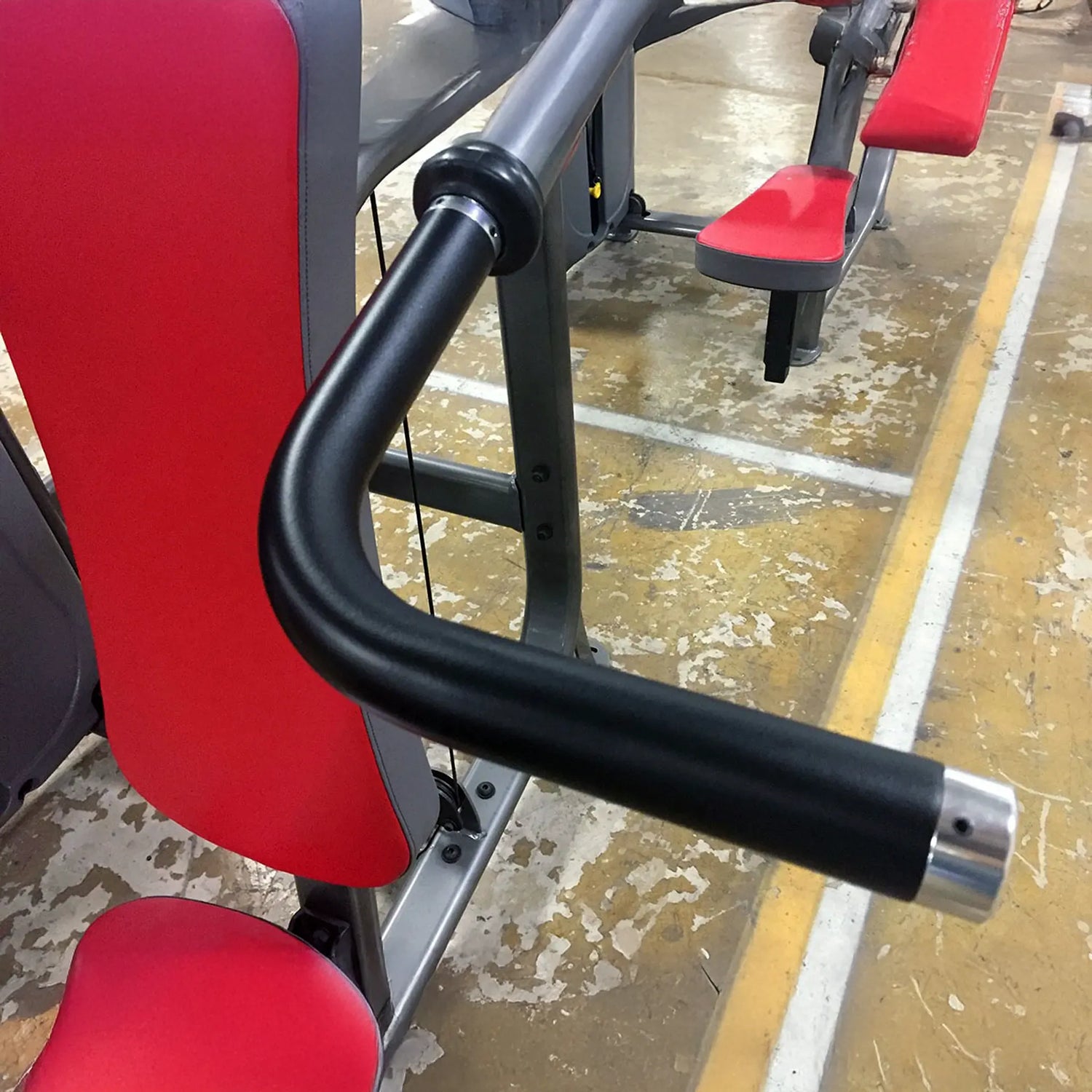Red gym machine pads with black metal handles on a concrete floor.