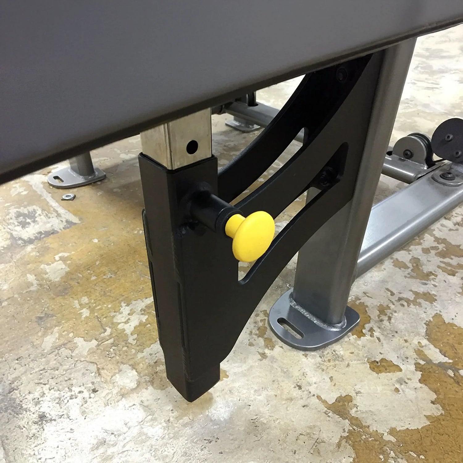 Close-up of a mechanical component with a yellow knob on a concrete floor.