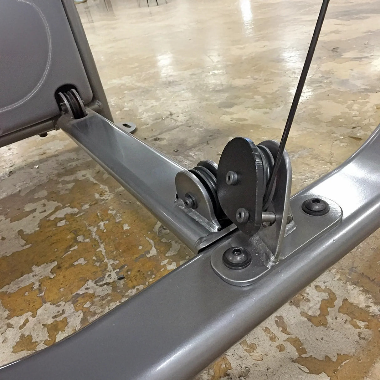 Metal pulley system mounted to a gray metal frame on a wooden floor
