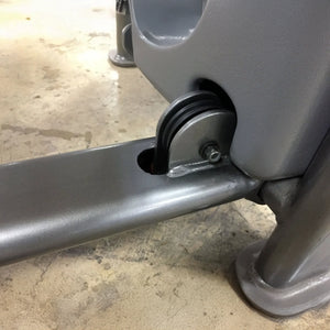 Close-up of a metal component on a piece of exercise equipment with a concrete floor background.