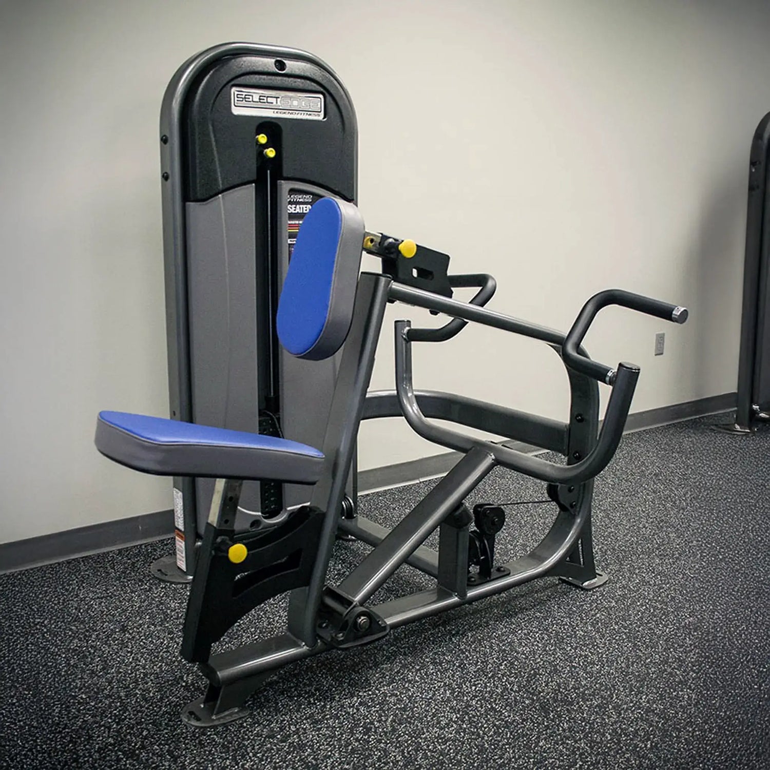 Gym machine with blue padding on a gray floor against a white wall