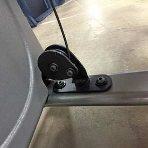 Close-up of a mechanical component on a gym machine with a black pulley and cable