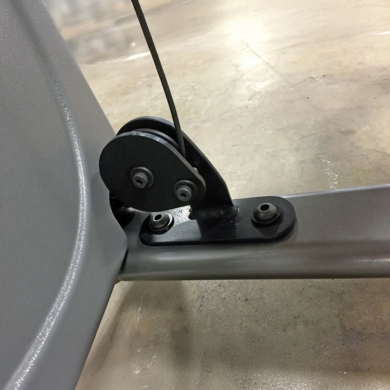 Close-up of a mechanical component on a gym machine with a black pulley and cable