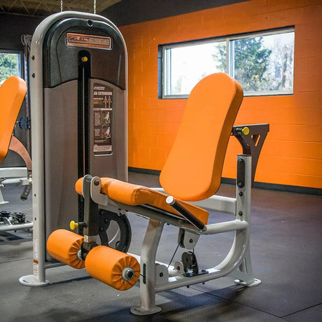 Gym machine with orange seat and padding in a room with orange walls and large windows.