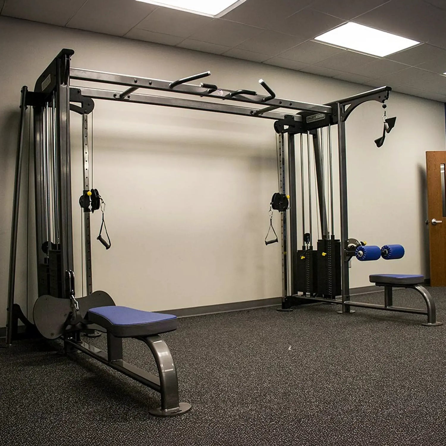 Gym equipment including a pull-up bar and weight bench in a room with beige walls and a door.