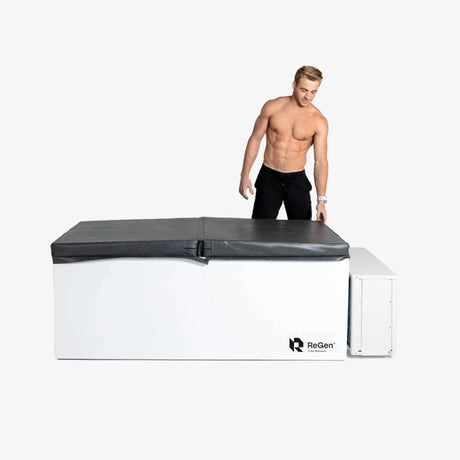 A rectangular cold plunge with a white exterior and a black foldable foam cover on top and a white external chiller unit on the right side of the plunge. There is a man standing behind the plunge with one hand on the cover about to pull it off.