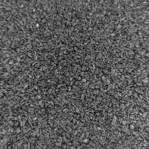 A close-up of ECORE Athletic's ECORE Rubber Pavers (1-3/4", 44.5 mm) shows a rough, textured dark gray surface with scattered small pebbles and irregular patterns, resembling asphalt or coarse concrete.