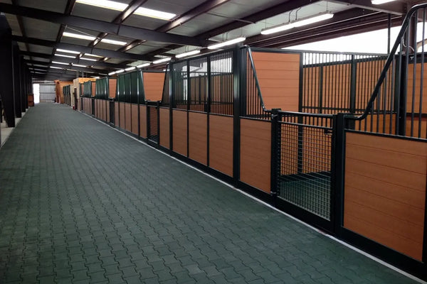 A dark long alley with a green floor made of rubber pavers running through a barn