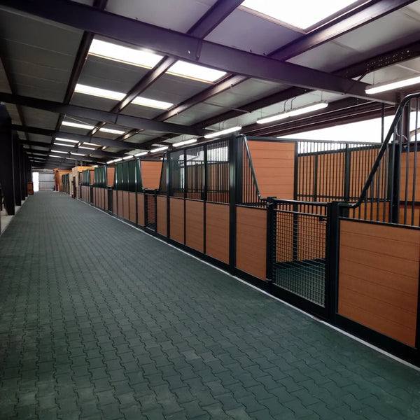 A dark long alley with a green floor made of rubber pavers running through a barn