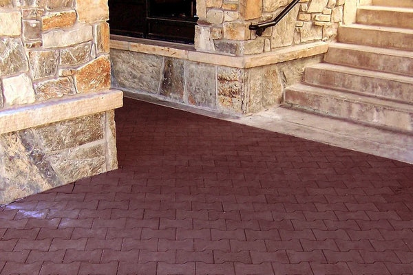 Red rubber paver patio leading up to a stone house and staircase