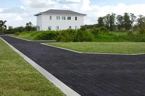 Long black rubber paver driveway with a white house and green grass in the countryside