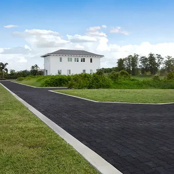 Long black rubber paver driveway with a white house and green grass in the countryside